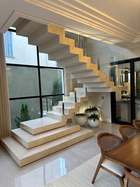 Com degraus plissados, patamares irregulares e revestida de mármore, a escada se destaca na área social | Projeto Meneghisso & Pasquotto Arquitetura | Foto: Divulgação